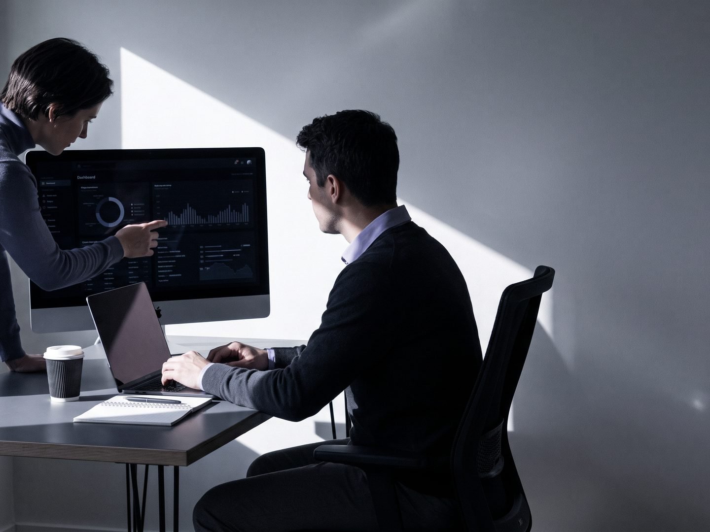 Two colleagues at a desk reviewing customer analytics on a dashboard.
